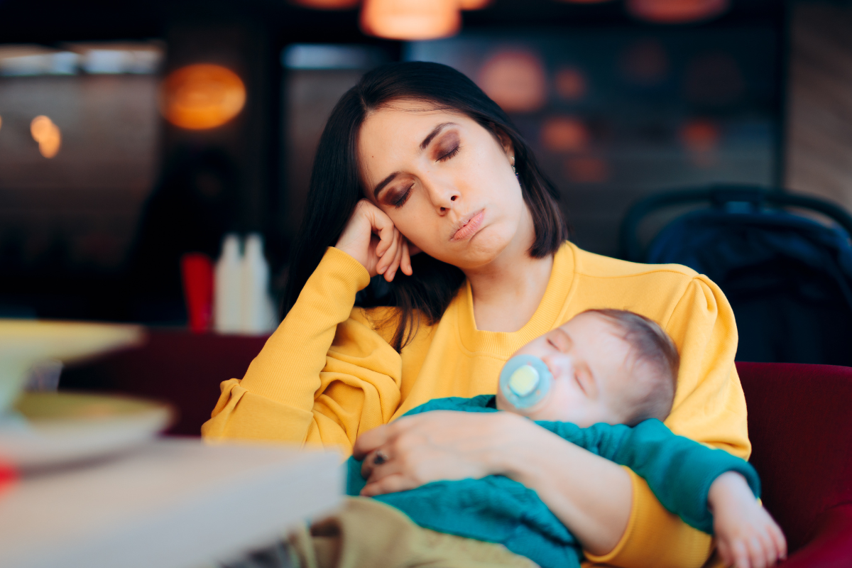 Erschöpfte Mutter mit schlafendem Baby im Arm