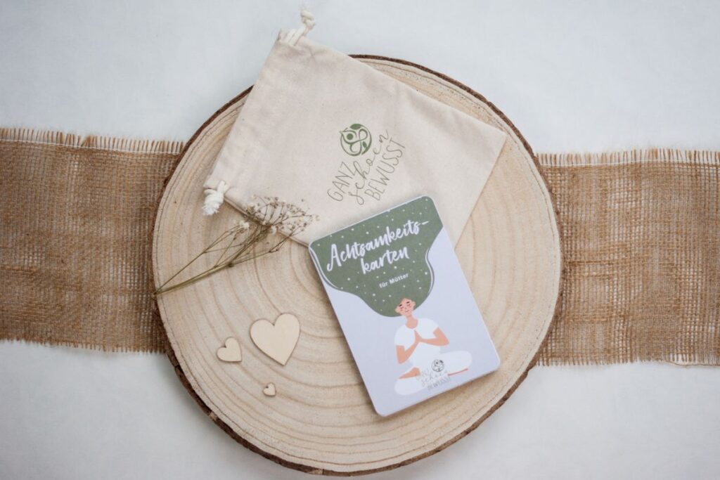 Ein Päckchen Achtsamkeitskarten für Mütter liegt auf einer Holzscheibe